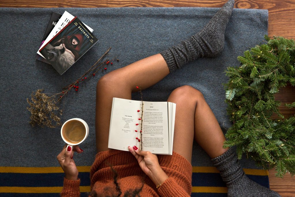 A bird's eye view of a person reading with a book in their lap and a coffee in their free hand.